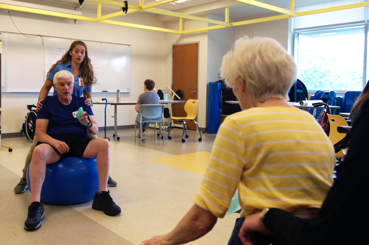 older adults on exercise balls with college student in background